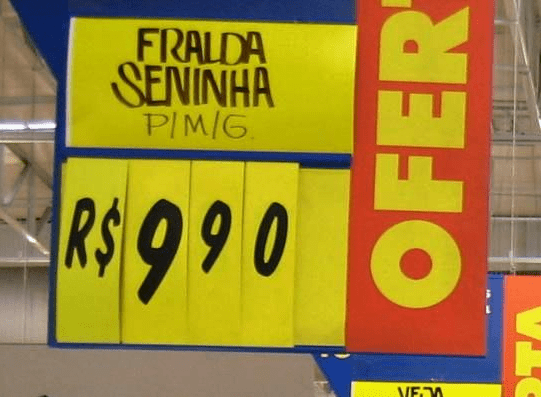 Placa do supermercado Extra com o texto: 'Fralda Seninha, R$9,90'.
O cifrão possui um único traço.